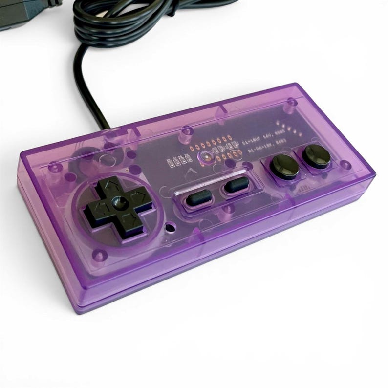Op de afbeelding: Een transparante paarse videogamecontroller met zwarte knoppen en een directioneel pad. De controller heeft een doorzichtige plastic behuizing, waardoor de interne componenten zichtbaar zijn. Een zwarte kabel loopt vanaf de bovenkant van de controller.