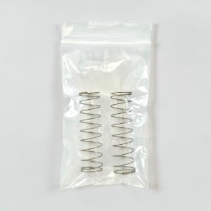 Op de afbeelding: Twee zilverkleurige spiraalveren in een doorzichtige plastic zak. De veren zijn strak gewikkeld en hebben een consistente spiraalvorm. De zak is verzegeld en ligt tegen een witte achtergrond.