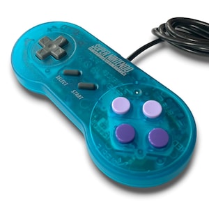May include: A transparent teal Super Nintendo controller with a black cable. The controller has gray directional buttons, gray select and start buttons, and four colored buttons: two lavender and two purple. The text "SUPER NINTENDO ENTERTAINMENT SYSTEM" is visible.