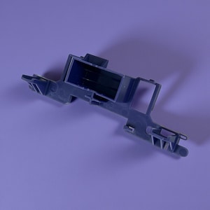 Könnte beinhalten: Ein blau-graues Kunststoffteil mit einem rechteckigen Mittelteil und verschiedenen hervorstehenden Armen und Laschen. Das Teil scheint ein mechanisches Bauteil zu sein, möglicherweise für ein Gerät oder eine Maschine, vor einem violetten Hintergrund.