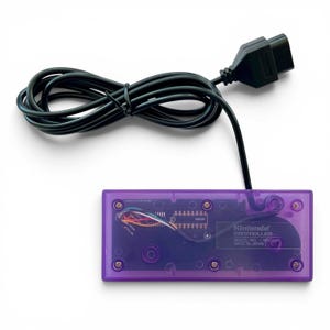 Op de afbeelding: Een transparante paarse Nintendo-controller met een zwarte kabel en connector. De interne componenten van de controller zijn zichtbaar. De tekst "Nintendo Controller" en "Made in Japan" staan op de controller.