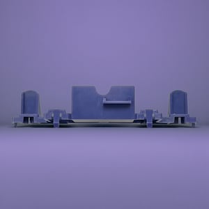 Op de afbeelding: Een blauw plastic onderdeel met een rechthoekig middengedeelte, een gebogen uitsparing en een klein plankje. Aan weerszijden bevinden zich twee staande secties, met extra structurele elementen. Het object staat tegen een paarse achtergrond.