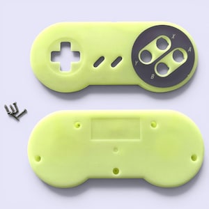 Könnte beinhalten: Ein zweiteiliges, limettengrünes Videospiel-Controllergehäuse mit einem grauen Knopfgruppensatz. Das Oberteil hat ein Steuerkreuz und drei kleine Tasten. Das Unterteil ist ein fester Rechteck. Kleine Schrauben sind sichtbar.