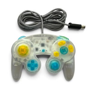 May include: A transparent video game controller with a clear shell, featuring yellow and blue buttons, joysticks, and a directional pad. The controller is attached to a long, black and white chevron-patterned braided cable with a black connector.