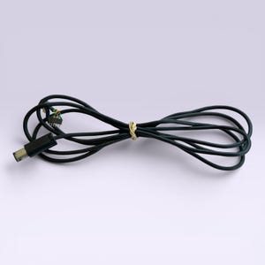 May include: A black USB cable with a male connector on one end and exposed wires on the other. The cable is looped and secured with a tan rubber band. The background is a solid, light purple.