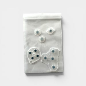 Puede incluir: Una bolsa de pl&aacute;stico transparente que contiene varios reemplazos de botones de mando de juego blancos y grises. Los botones son de varias formas y tama&ntilde;os, incluidos dise&ntilde;os circulares y de almohadilla direccional. La bolsa est&aacute; sellada con un cierre de cremallera.