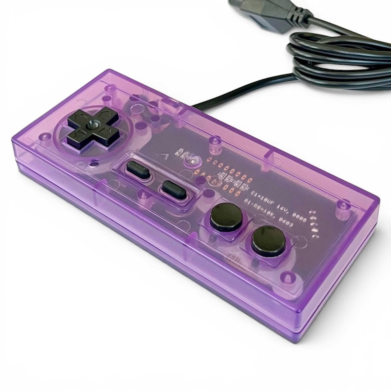 Op de afbeelding: Een transparante paarse gamecontroller met zwarte knoppen en een navigatiepad. De controller heeft een rechthoekige vorm en een zwarte kabel. De interne bedrading is zichtbaar door het doorschijnende plastic.