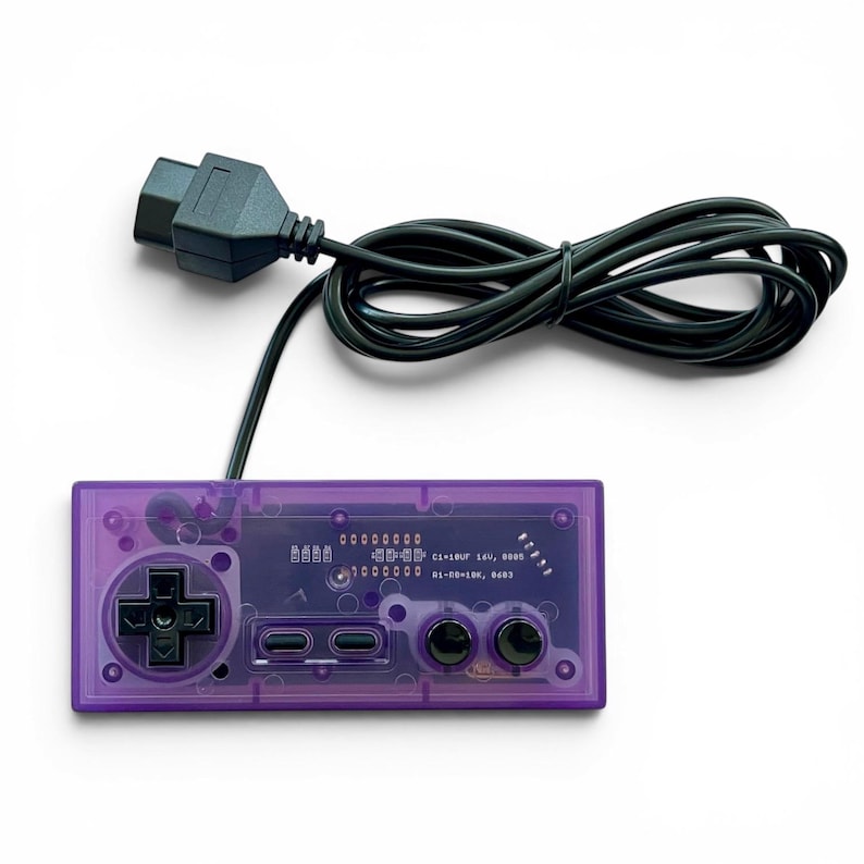 Op de afbeelding: Een transparante paarse videogamecontroller met een zwarte directionele pad, knoppen en een zwarte kabel. De controller heeft een retro-ontwerp, met zichtbare interne componenten. De kabel is aangesloten op een zwarte voedingsadapter.