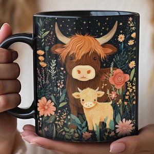 May include: Black ceramic mug featuring a Highland cow and calf amidst a floral design. The artwork includes a dark background with stars, brown and yellow cows, and orange and pink flowers. The mug has a black handle.