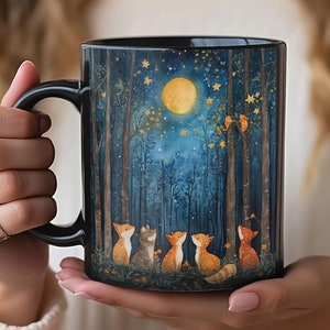 May include: Black ceramic mug with a whimsical illustration of foxes looking up at a full moon in a starry forest. The foxes are orange, brown, and white.