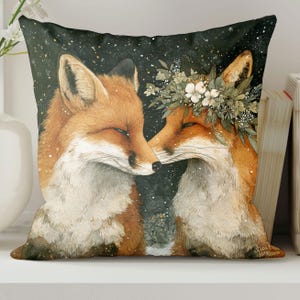 May include: Square decorative pillow featuring a watercolor illustration of two foxes. One fox wears a floral crown. The foxes are depicted with closed eyes, touching noses, against a dark background with white speckles.