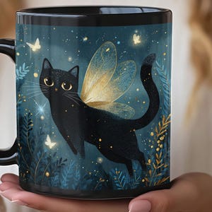 May include: Black ceramic mug featuring a whimsical illustration of a black cat with golden fairy wings, set against a dark teal background with butterflies and stars. The mug has a black handle and rim, perfect for a cat lover.
