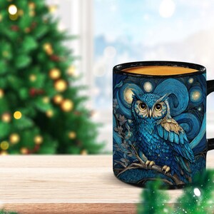 May include: A black ceramic mug featuring a detailed illustration of a blue owl perched on a branch against a swirling night sky background with circular yellow stars. The mug has a solid black handle and a black interior rim.