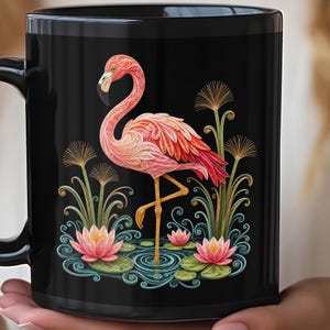 Könnte beinhalten: Ein schwarzer Keramikbecher mit einer detaillierten Grafik eines rosa Flamingos, der im Wasser zwischen rosa Lotusblüten und grünen Schilfrohren steht. Das Design verwendet komplexe, wirbelnde Muster, um den Flamingo und die floralen Elemente zu bilden.