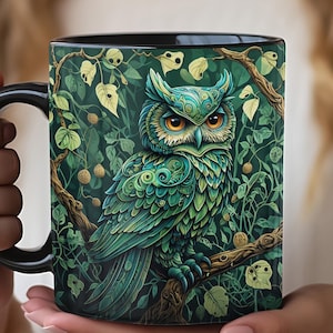 May include: A black coffee mug with a green and blue owl illustration. The owl is perched on a branch with green leaves and vines. The owl's eyes are yellow and its feathers are detailed with intricate patterns.