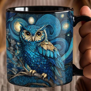 May include: A black ceramic mug featuring a detailed illustration of an owl perched on a branch. The owl has blue and gold feathers, large yellow eyes, and is set against a swirling dark blue background with glowing circular light patterns.