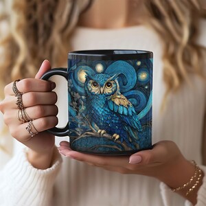 May include: A black ceramic mug featuring a detailed illustration of a blue owl perched on a branch against a swirling dark blue background with glowing yellow stars. The owl has large yellow eyes and textured blue and gold feathers.
