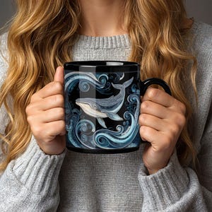May include: Black ceramic mug featuring a detailed illustration of a whale swimming in stylized blue waves. The whale is depicted in shades of gray and blue, set against a black background. The mug has a black handle.
