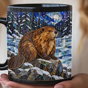 May include: A black ceramic mug featuring a vibrant, stained-glass style illustration of a brown beaver sitting on a rock. The background depicts a snowy winter forest scene with pine trees, a frozen river, and a full moon in a deep blue sky.