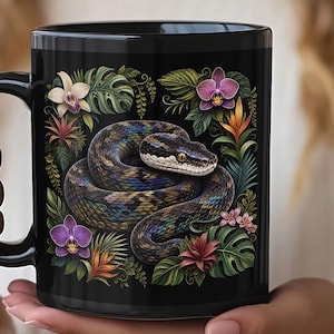 May include: A black ceramic mug featuring a coiled snake with iridescent scales surrounded by a vibrant arrangement of tropical flowers and green monstera leaves. The snake is positioned in the center, framed by purple, pink, and orange orchids.