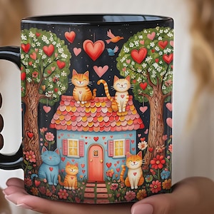 May include: A black ceramic mug featuring a colorful illustration of a light blue house with a pink roof, surrounded by two large trees, flowers, and four cats. Red hearts and small birds are scattered throughout the dark night sky background.