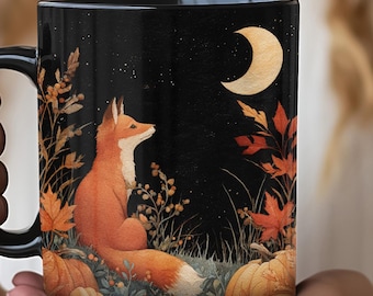 May include: A black ceramic mug featuring a printed illustration of an orange fox sitting in a field of autumn foliage and pumpkins under a night sky with a crescent moon and stars. The design wraps around the exterior of the cylindrical vessel.