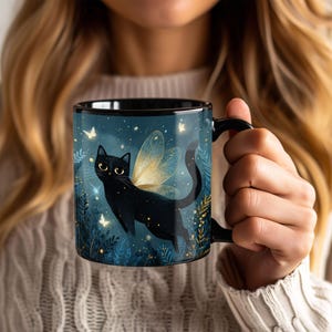 May include: Black ceramic mug featuring a whimsical illustration of a black cat with golden fairy wings, set against a dark blue background with stars and butterflies. The mug has a black handle and rim, perfect for coffee or tea.