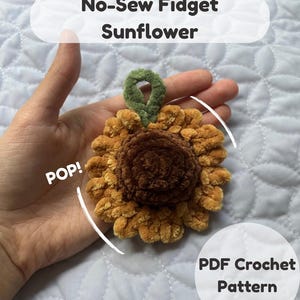 May include: A plush sunflower fidget toy made of soft brown and golden yellow yarn with a green loop at the top. The text on the image reads No-Sew Fidget Sunflower, POP!, and PDF Crochet Pattern. This item is a digital guide for crafting.