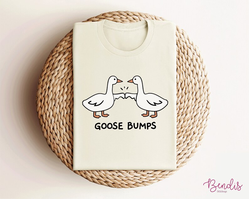 May include: A light beige t-shirt with a graphic of two cartoon geese bumping fists. The text "GOOSE BUMPS" is printed below the geese.