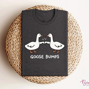 May include: A dark gray t-shirt with a white graphic of two geese bumping into each other. The text "Goose Bumps" is printed below the geese.