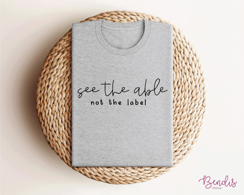 K&ouml;nnte beinhalten: Graues T-Shirt mit dem Text "see the able not the label" in schwarzer Schrift.