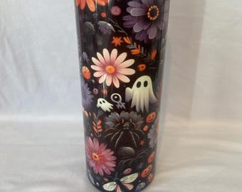 May include: A tall, insulated tumbler with a floral and Halloween design. The tumbler features orange, pink, and purple flowers, along with white ghost illustrations, set against a dark background. The tumbler has a purple lid.