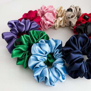 Peut inclure: Collection de chouchous en satin de différentes couleurs, dont le violet, le vert, le bleu, le rose, le rouge et le beige. Chaque chouchou est froncé et a un aspect doux et brillant. Certains chouchous ont une petite étiquette noire avec une lettre blanche.