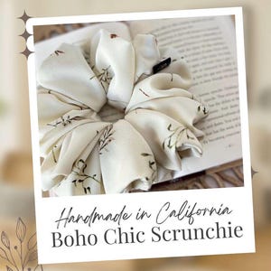 May include: Cream-colored scrunchie with a floral pattern. The fabric is gathered and voluminous, with small brown leaf-like designs. The scrunchie is handmade in California. The text "Boho Chic Scrunchie" is also visible.
