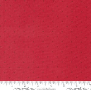 May include: A red fabric featuring a repeating pattern of small, dark red polka dots. A white ruler is positioned along the bottom edge, showing measurements in inches, with the text 'moda' and 'www.modafabrics.com' printed on the ruler.