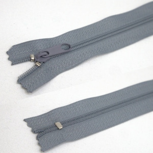 Könnte beinhalten: Ein grauer Reißverschluss, offen und geschlossen dargestellt, mit passendem Zipper. Die Metallzähne sind silberfarben. Das Stoffband ist einfarbig mittelgrau. Geeignet für Kleidung oder Stoffprojekte.