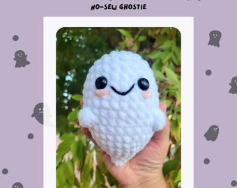 May include: White crocheted ghost with a smiling face and black eyes. The ghost is being held in a hand. The background is a purple color with a pattern of gray ghosts.