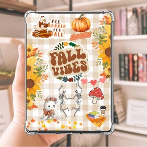 Peut inclure: Une coque de tablette transparente ornée d'autocollants sur le thème de l'automne. Le design comprend une citrouille, des tournesols et le texte "FALL VIBES". D'autres autocollants représentent un canard lisant, des squelettes dansant et un champignon.