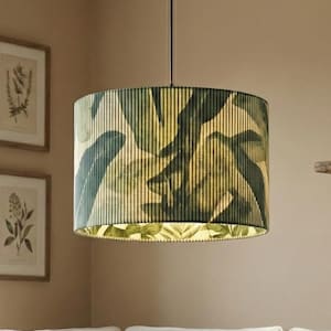 Peut inclure: Un luminaire suspendu cylindrique avec un motif de feuilles vertes et jaunes est suspendu au-dessus d'un canapé d'angle blanc. La pièce comprend une table basse en bois, des coussins décoratifs et des estampes botaniques encadrées.