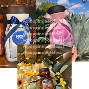May include: Three ceramic jars with a floral design and the word "MADRE" on them. The jars are decorated with blue and pink ribbons and are filled with a brown liquid. The jars are sitting on a table with a bouquet of flowers.