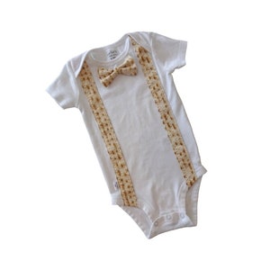 May include: White baby onesie with a bow tie and suspenders made of matzah. The onesie has the text "Little Man" on the tag.