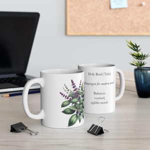 May include: Two white ceramic mugs. One mug features a botanical illustration of holy basil with purple flowers and green leaves. The other mug has text that reads "Holy Basil (Tulsi) Adaptogen for modern stress. Balances cortisol, uplifts mood."