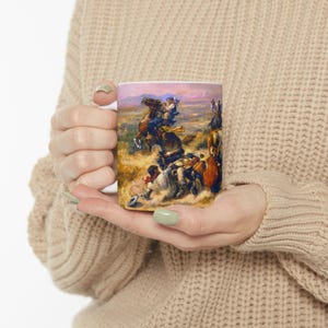 Könnte beinhalten: Weiße Keramik-Tasse mit detaillierter Malerei einer historischen Szene mit Cowboys auf Pferden. Das Kunstwerk zeigt eine dynamische Actionszene mit Figuren in Bewegung, vor einer Landschaft mit rosa Himmel.