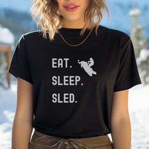 Puede incluir: Camiseta negra con texto blanco que dice "Comer. Dormir. Trineo." y una silueta de una persona conduciendo una moto de nieve.