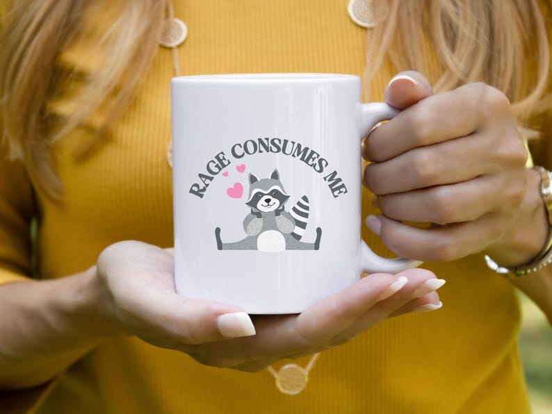 Peut inclure: Une tasse &agrave; caf&eacute; en c&eacute;ramique blanche avec une illustration de raton laveur noir et gris et le texte "Rage Consumes Me".