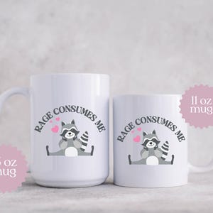 Peut inclure: Deux tasses en c&eacute;ramique blanche avec un graphique de raton laveur noir et gris et le texte "Rage Consumes Me". La tasse la plus petite est de 11 oz et la tasse la plus grande est de 15 oz.