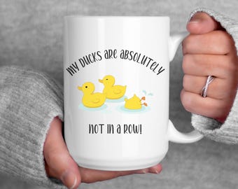 May include: White ceramic mug with a black graphic of three yellow rubber ducks. The text reads "My ducks are absolutely not in a row!"