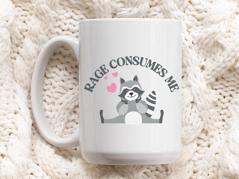 Peut inclure: Une tasse &agrave; caf&eacute; en c&eacute;ramique blanche avec une illustration de raton laveur noir et gris et le texte "RAGE CONSUMES ME".