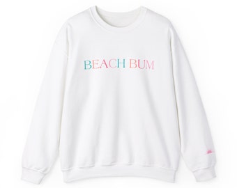 Può includere: Felpa bianca con il testo "BEACH BUM" in colori arcobaleno sul davanti. Un piccolo grafico di sole rosa è sulla manica destra.