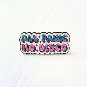 May include: A white enamel pin with the text "ALL PANIC NO DISCO" in blue and pink lettering. The letters are outlined in black and have a 3D effect.